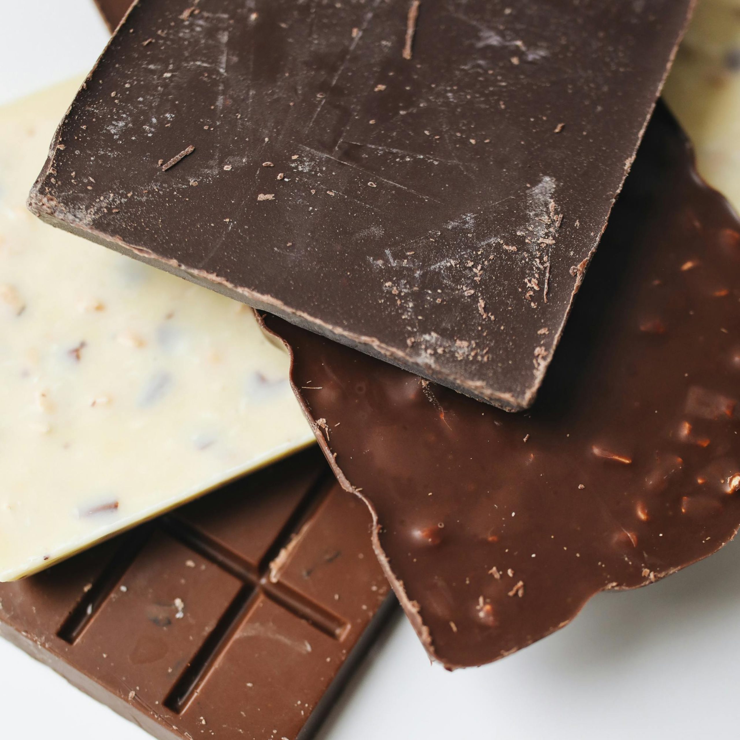 Variation von gebrochenen Schokoladentafeln in den Sorten weiße Schokolade, Vollmilch und Zartbitter übereinandergelegt