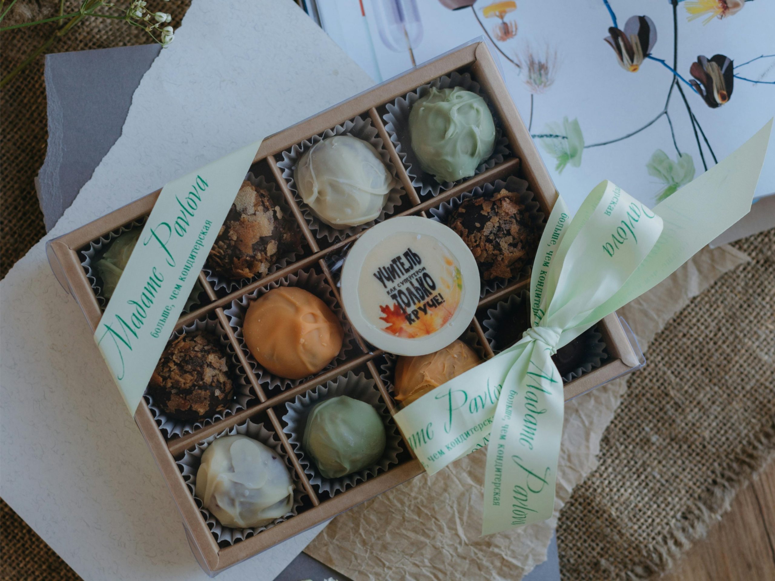 Rechteckige Geschenkbox 'Cacao Classique' mit transparentem Deckel, gefüllt mit hellen und dunklen Pralinenkugeln, gebunden mit einer hellgrünen Schleife