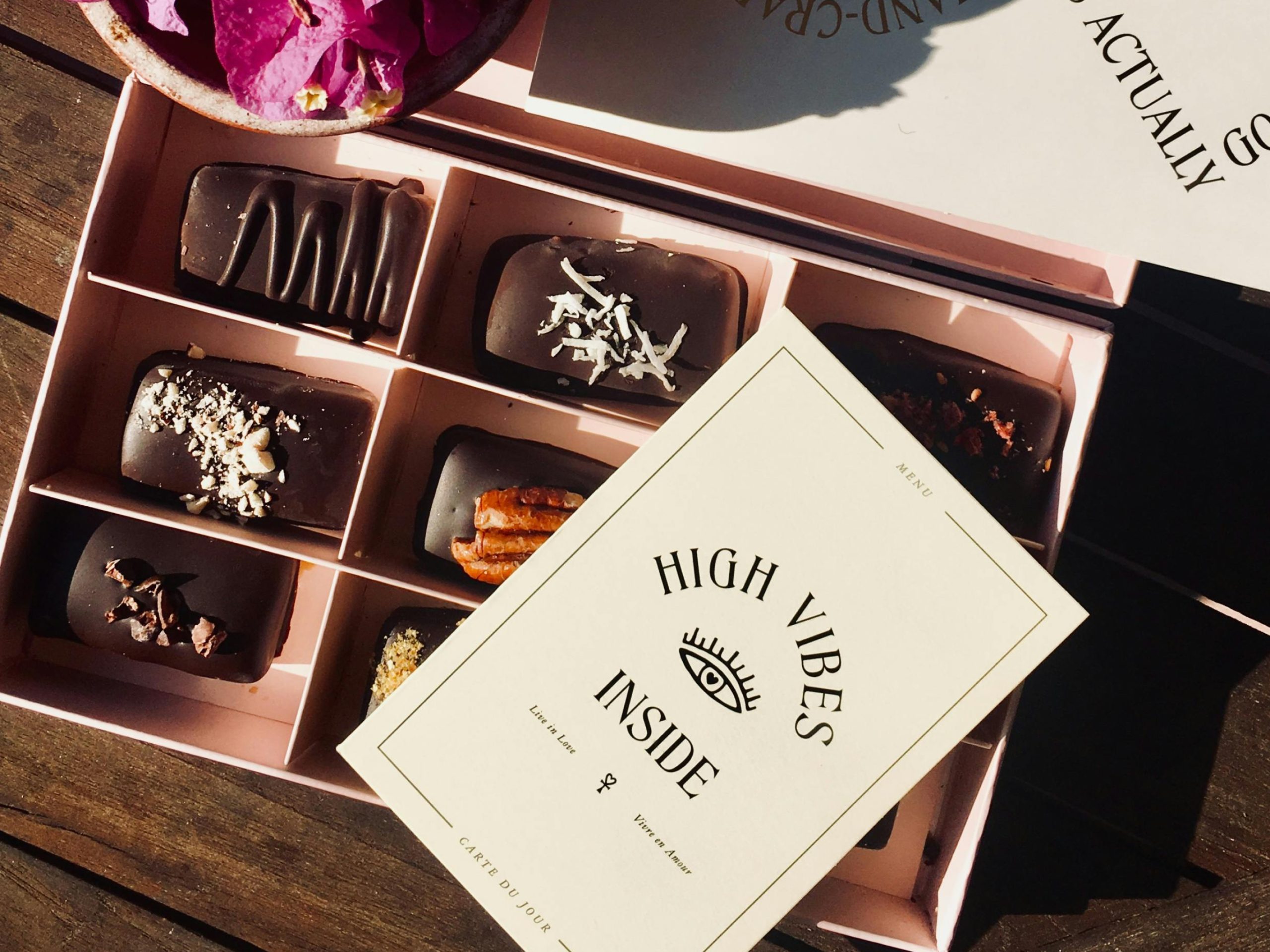 Geöffnete rosafarbene Schachtel 'Dark Temptation', gefüllt mit dunklen Schokoladen-Rechtecken und einer Einlegekarte mit der Aufschrift 'High Vibes Inside